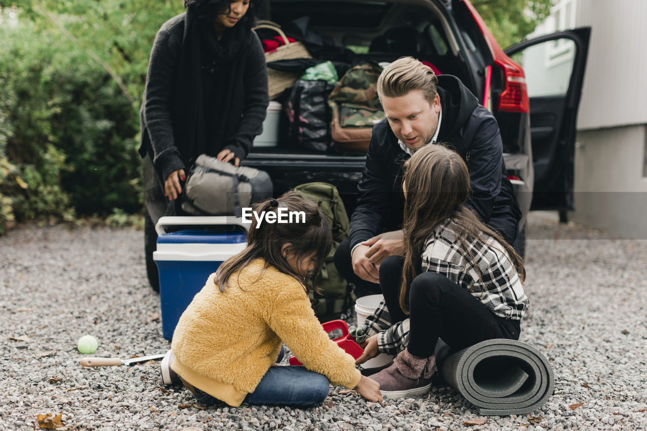 Father talking with daughters while loading luggage in car