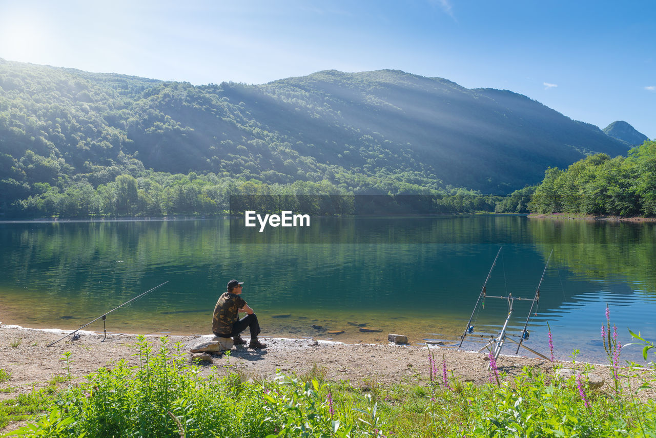 Man fishing on lake against mountain