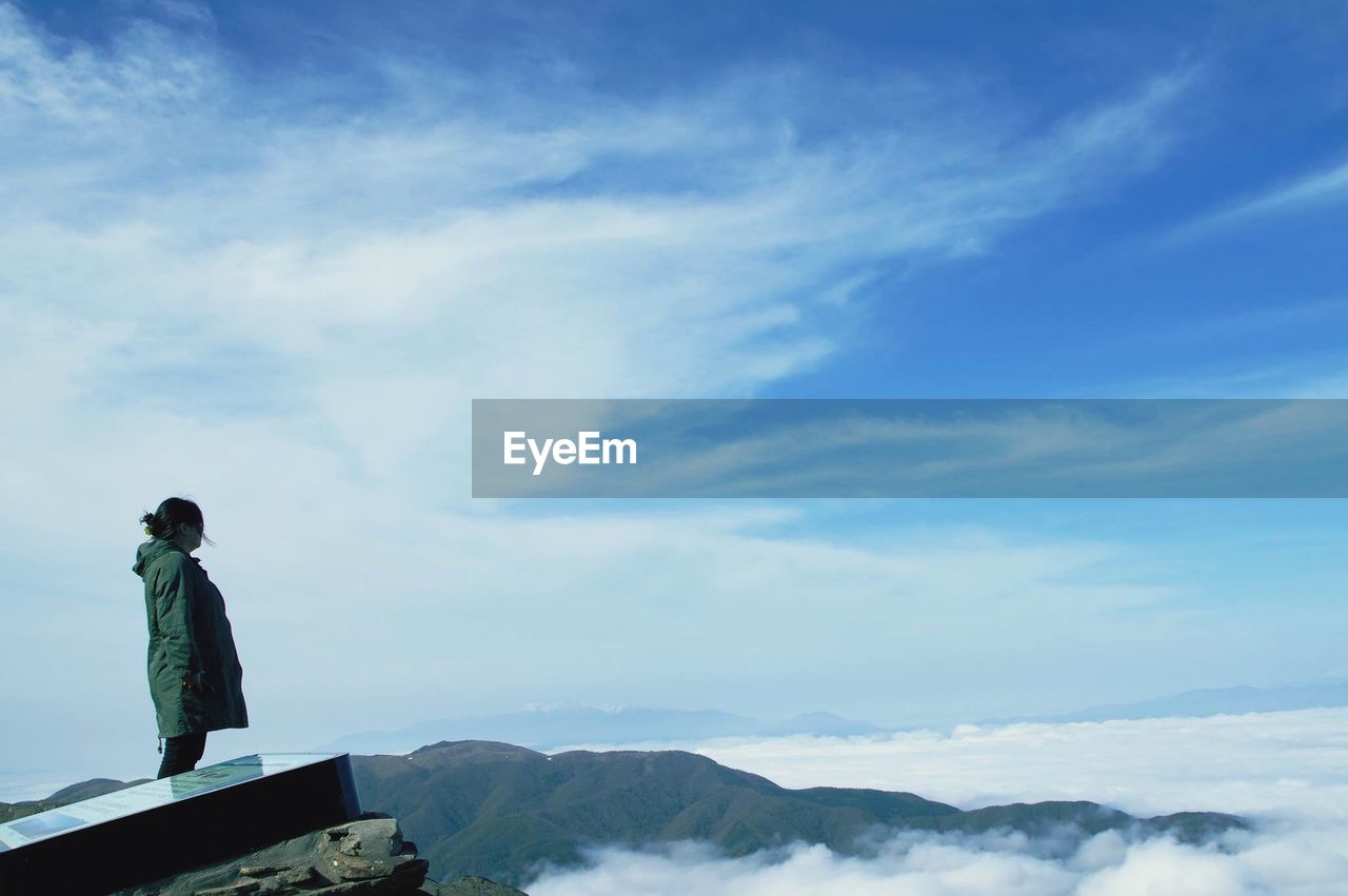 Side view of woman standing on mountain against sky