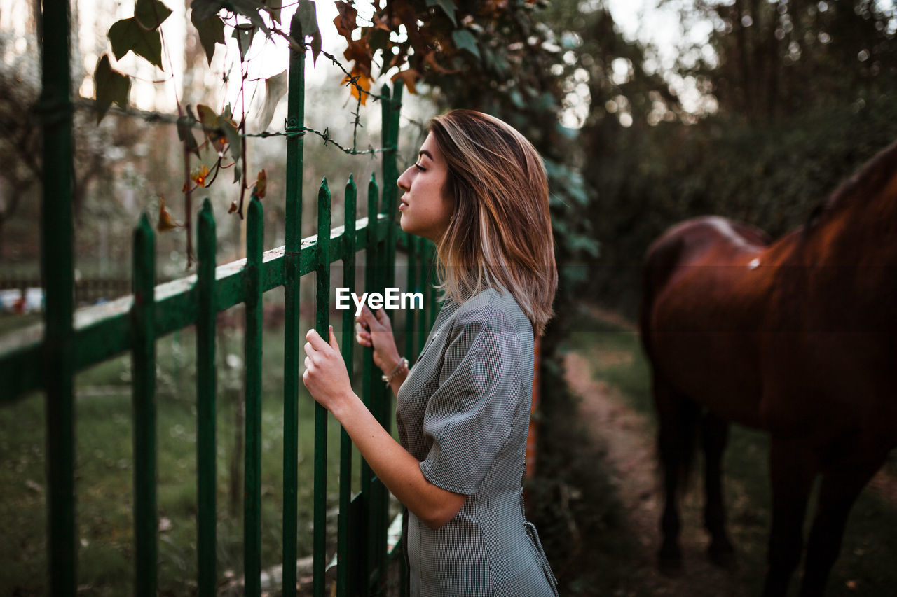 SIDE VIEW OF TEENAGE GIRL STANDING BY FENCE