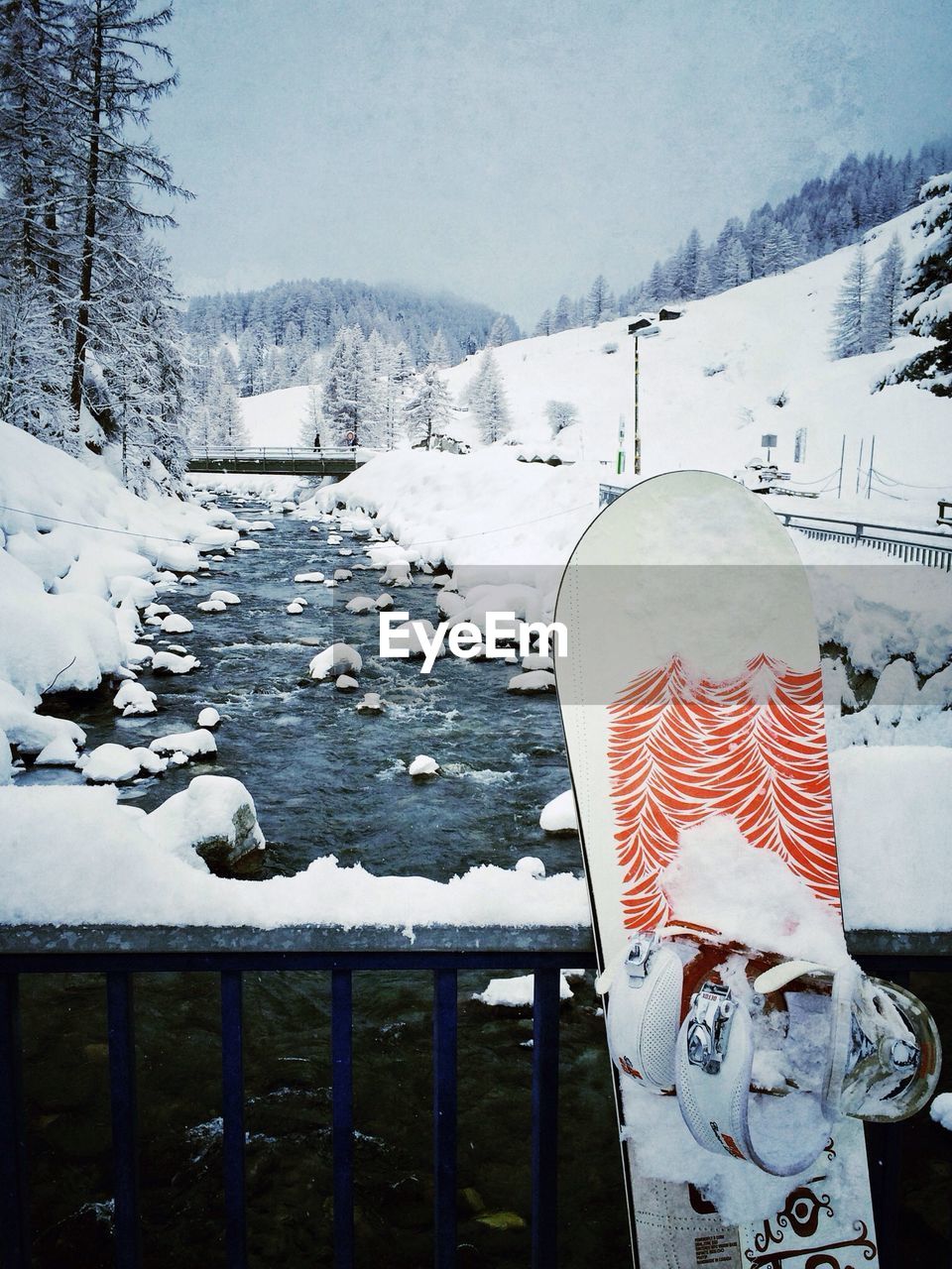 Snowboard against river in snow