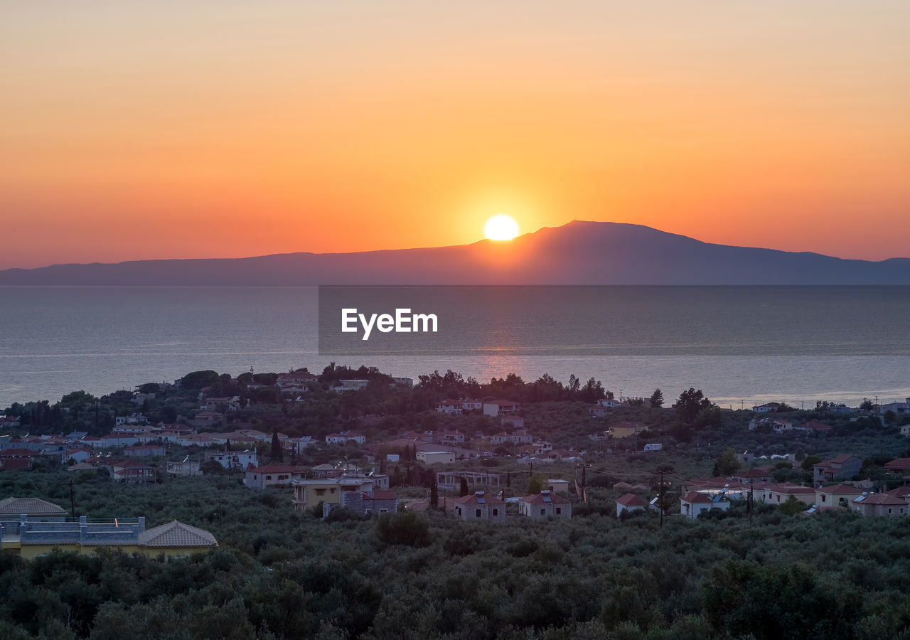 TOWNSCAPE BY SEA AGAINST ORANGE SKY