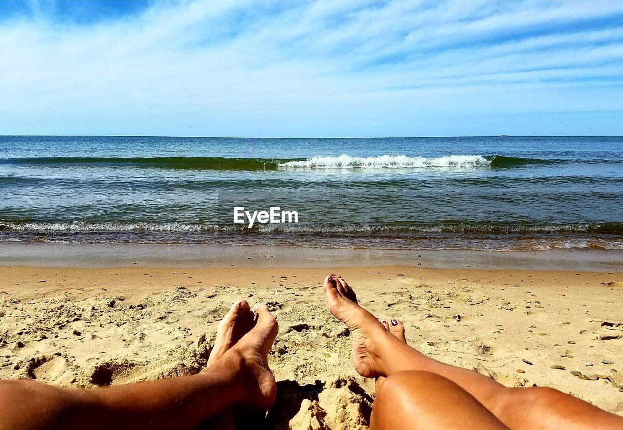 LOW SECTION OF PEOPLE AT BEACH AGAINST SKY