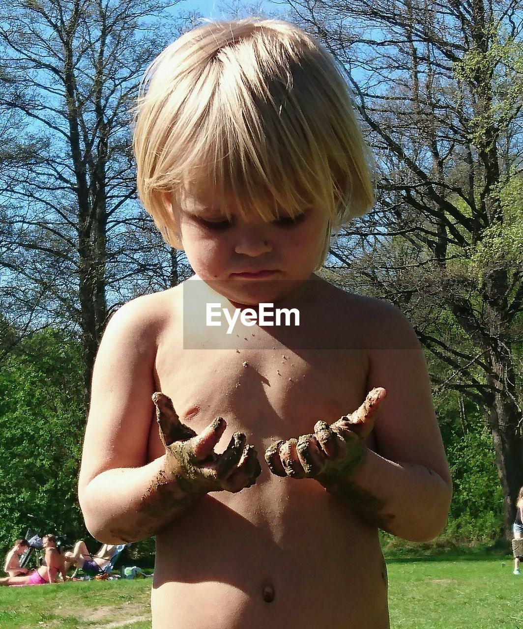 Close-up of shirtless girl looking at muddy hands