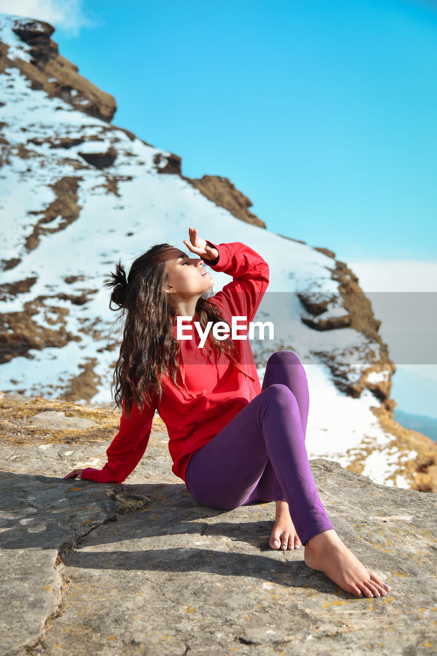 Full length of woman sitting on rocky mountain