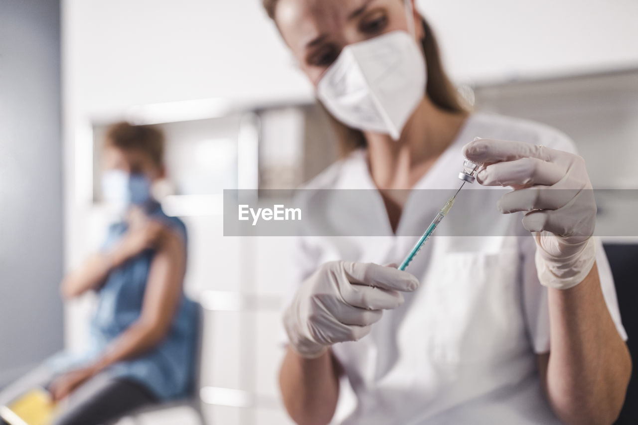 Nurse injecting syringe in vial at vaccination center