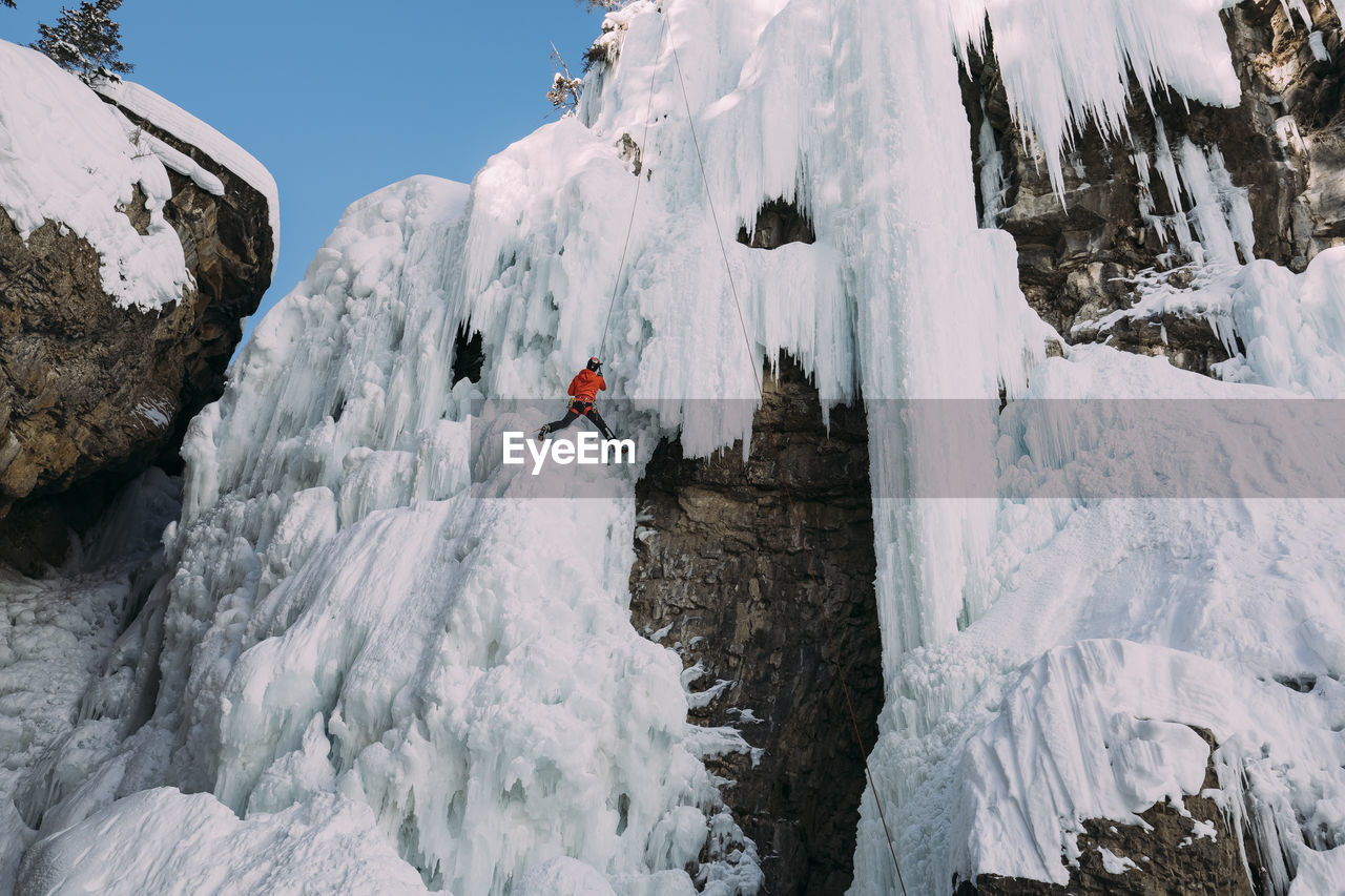 Low angle view of woman climbing on snowcapped mountain during winter