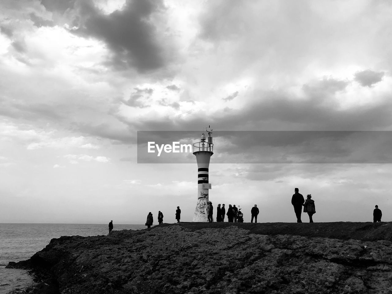 Silhouette people on beach by lighthouse against sky