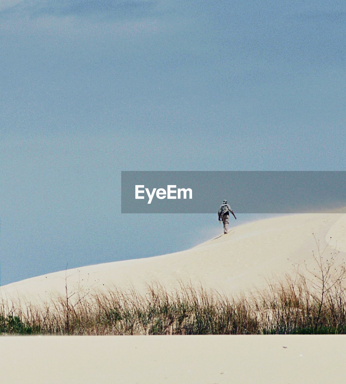 Man walking on sand dune against clear sky