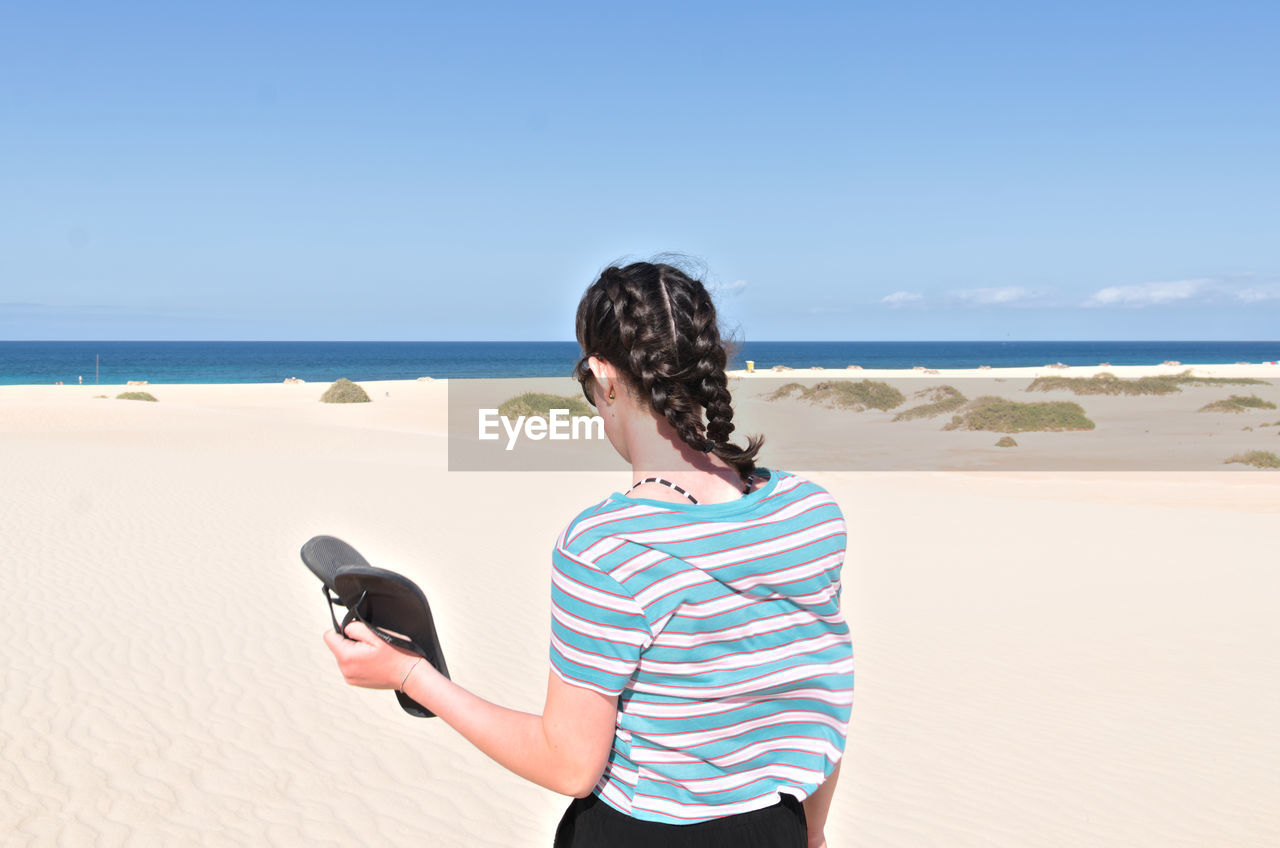 Rear view of teenage girl with braided hair standing on beach against sky