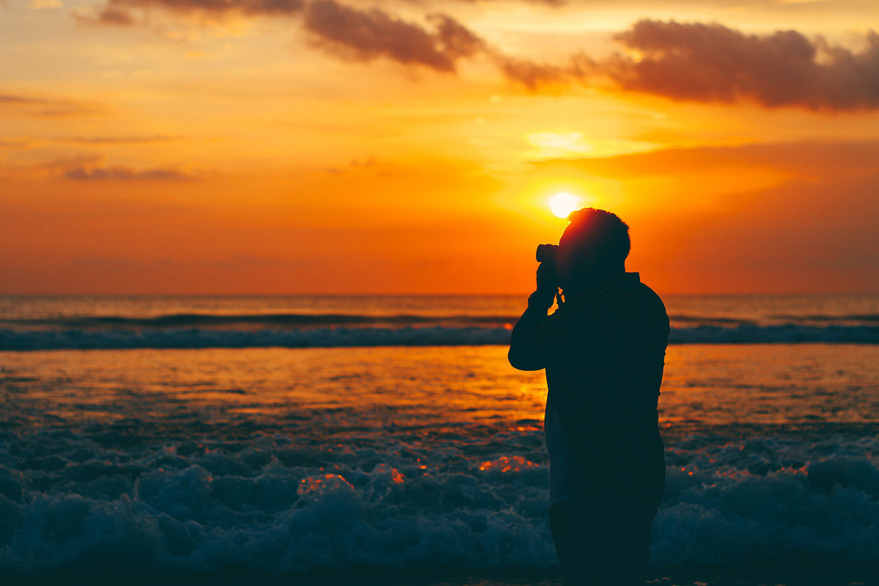 Silhouette man photographing on beach during sunset