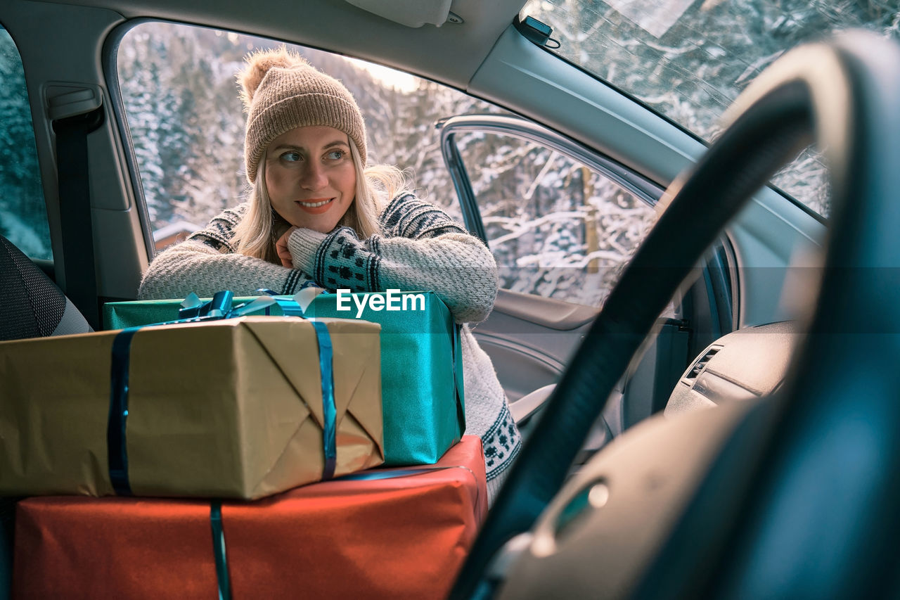 Woman giving gifts is holding presents delivering to home car holidays concept sunny cold winter day