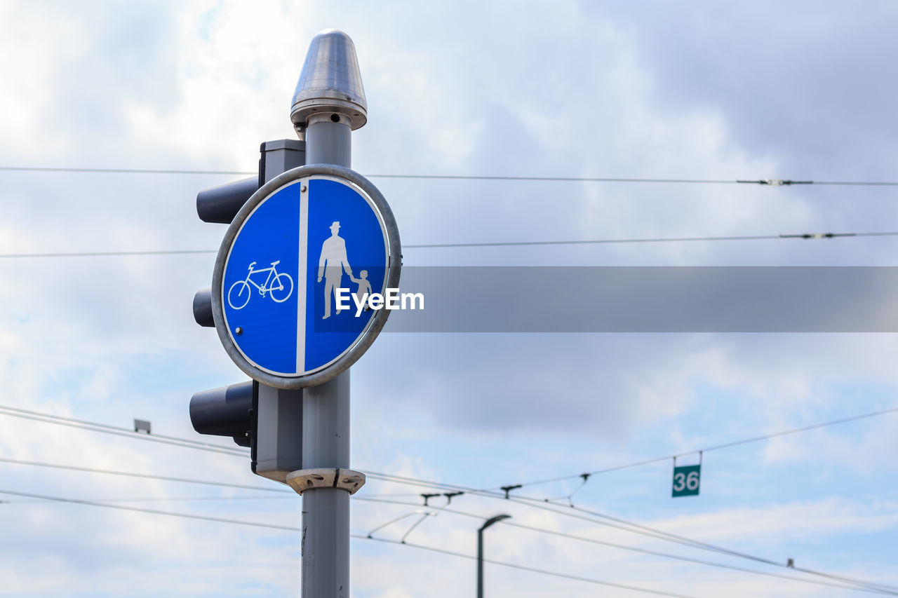 cloud, sign, sky, communication, blue, road, road sign, lighting, guidance, light fixture, street light, day, low angle view, no people, nature, traffic light, cable, transportation, symbol, technology, street sign, signage, traffic sign, outdoors, electricity, city, signaling device, street, pole, directional sign, architecture, information sign, arrow symbol, power line