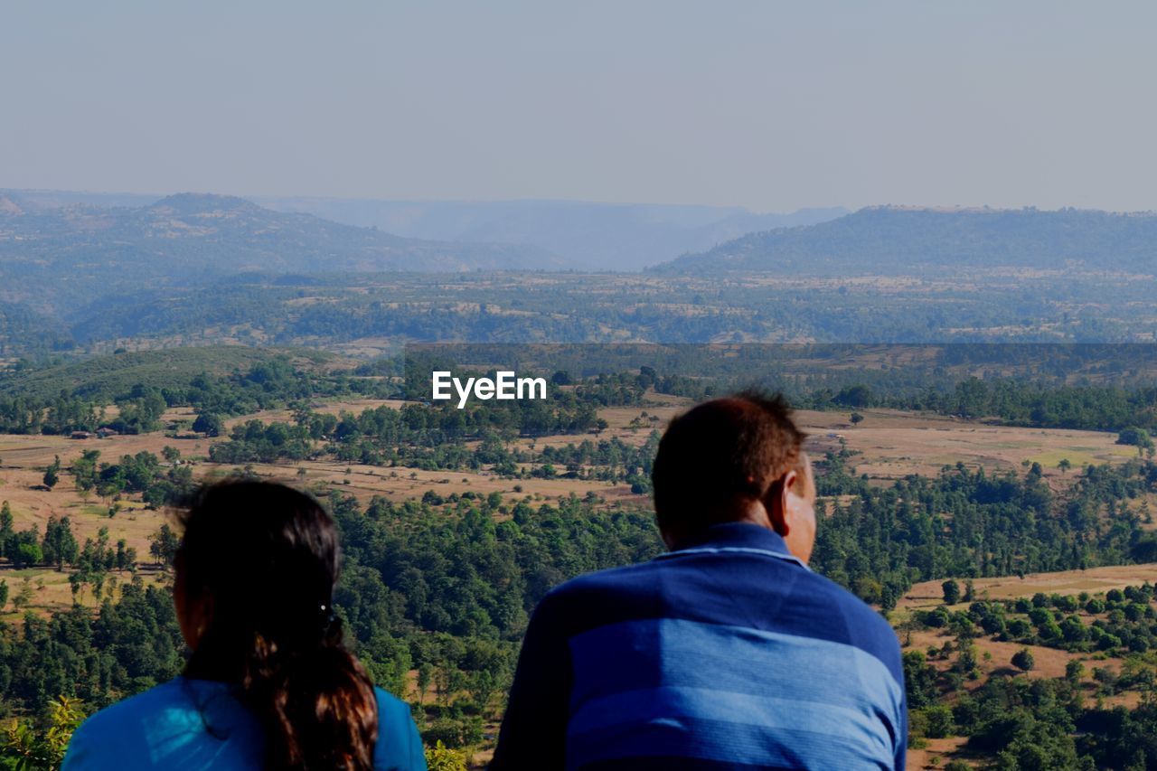 REAR VIEW OF PEOPLE LOOKING AT MOUNTAIN LANDSCAPE