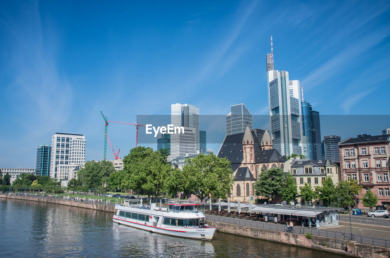 BOATS IN RIVER BY BUILDINGS AGAINST SKY