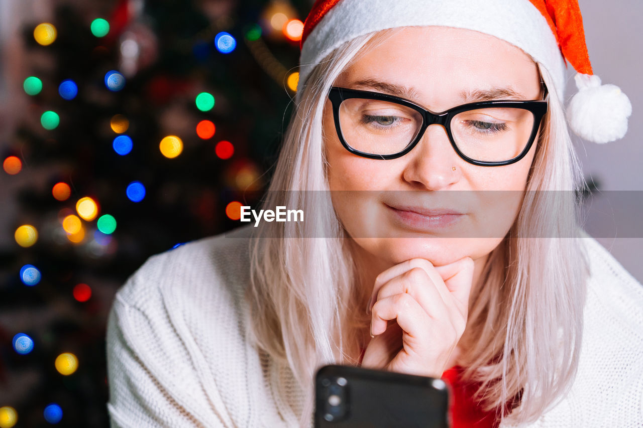 Smiling woman using mobile phone against illuminated christmas tree