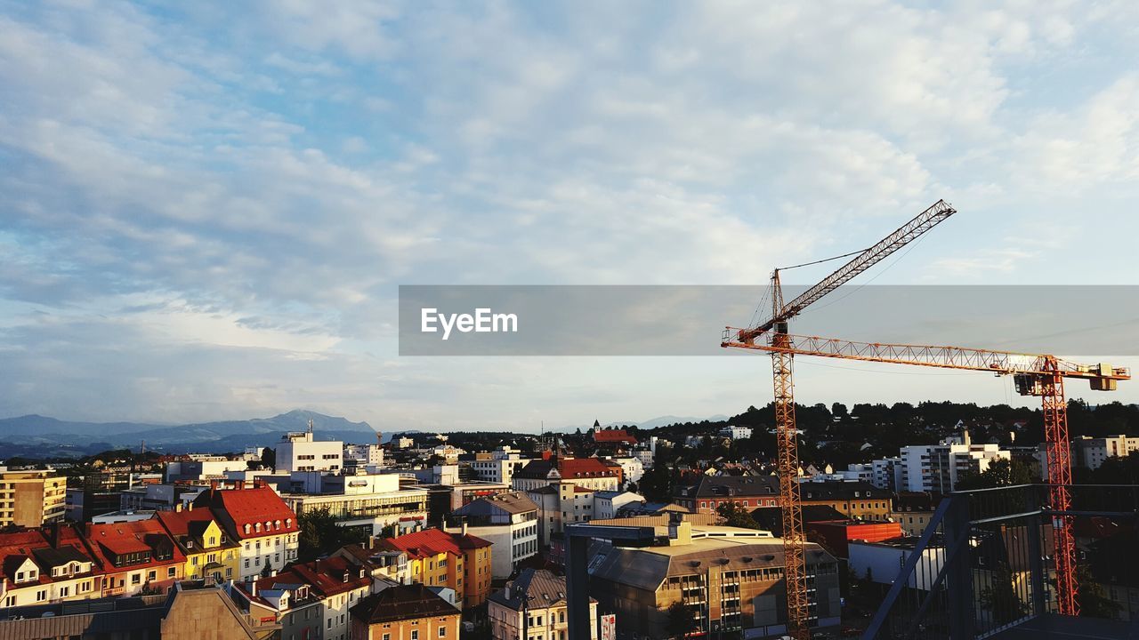 Cranes by buildings in city against sky