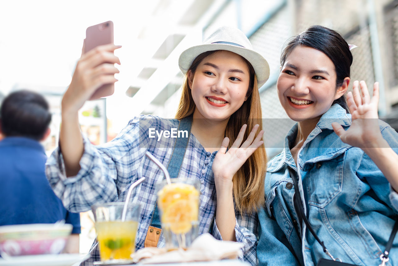 PORTRAIT OF SMILING YOUNG WOMAN USING PHONE WHILE LOOKING AWAY