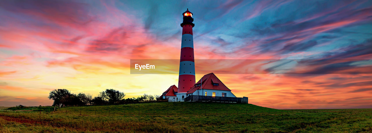 Lighthouse on field against sky during sunset