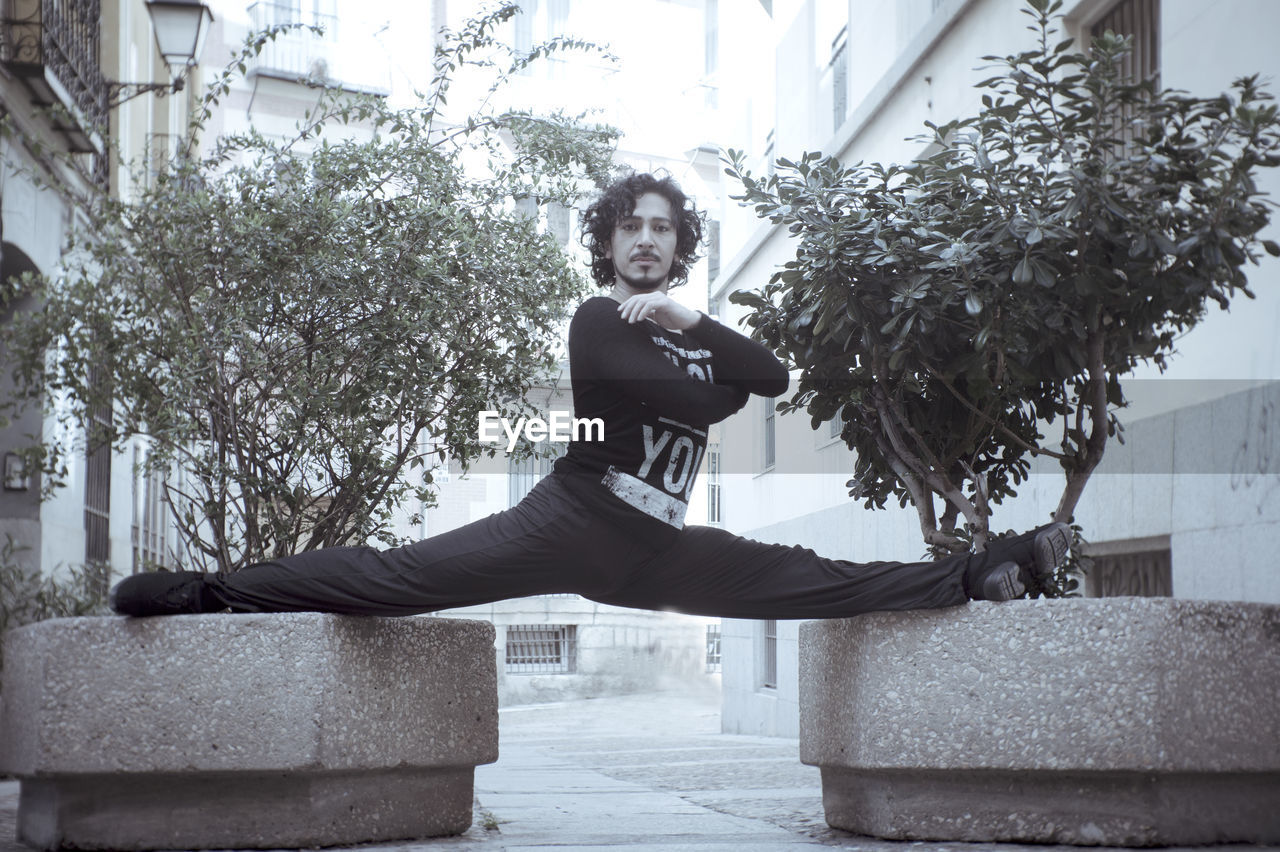 Full length portrait of man with legs apart balancing on retaining walls in city