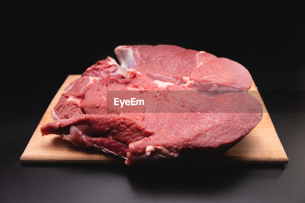 Piece of raw beef in a slice on a wooden cutting board, on a black background. procuring food