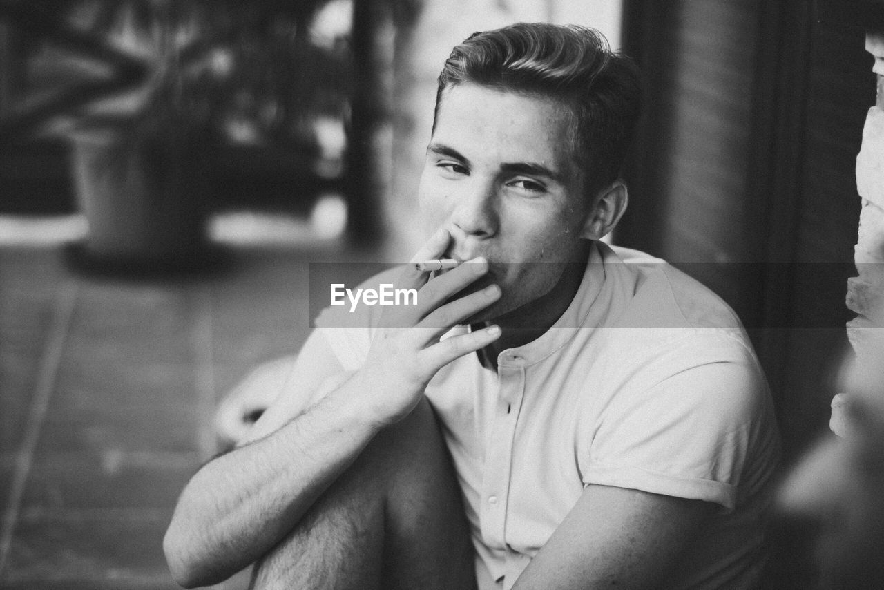 Young man smoking while sitting at entrance