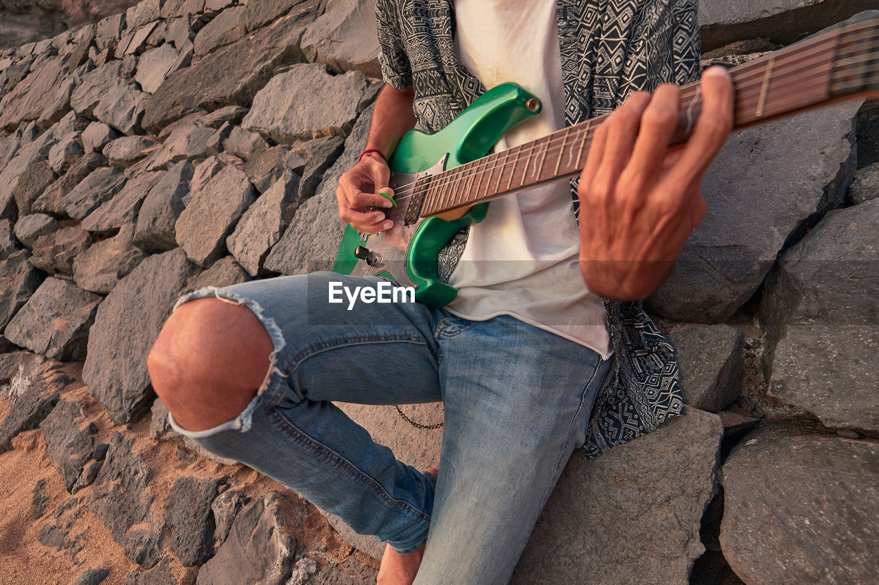 Midsection of man playing guitar while standing by rocks