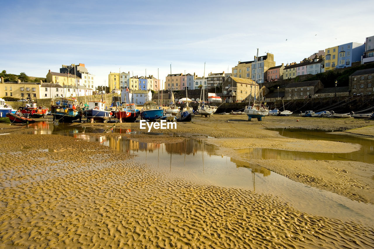 Boats moored on beach by buildings against sky