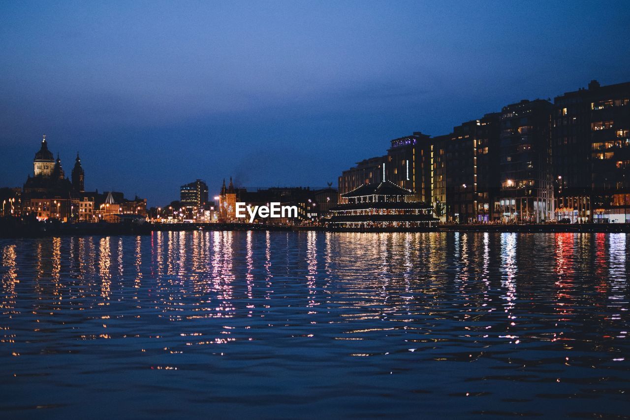 RIVER BY ILLUMINATED BUILDINGS AGAINST SKY AT NIGHT