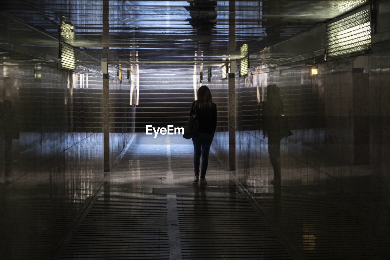 Rear view of woman walking in illuminated tunnel