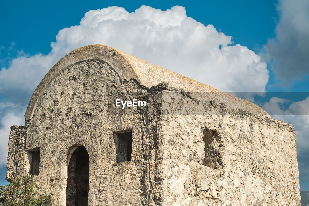 An abandoned greek chapel against a blue sky with clouds is located on a mountain 