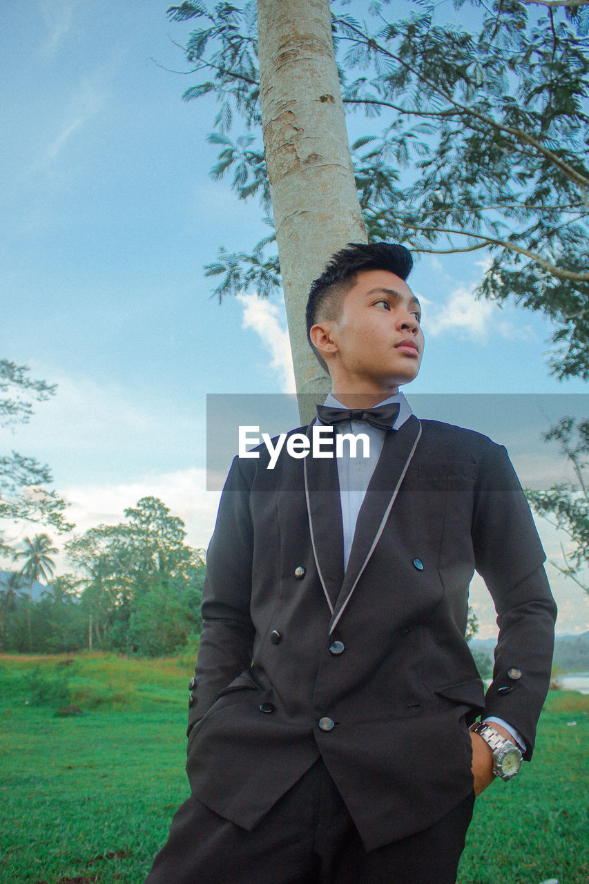 Boy in suit standing against tree