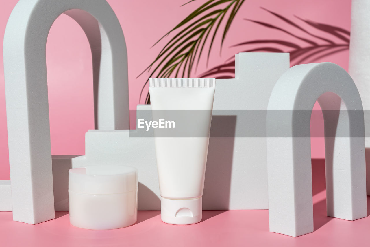 White blank cosmetic product bottles on pink background with palm branch, as advertisement. 