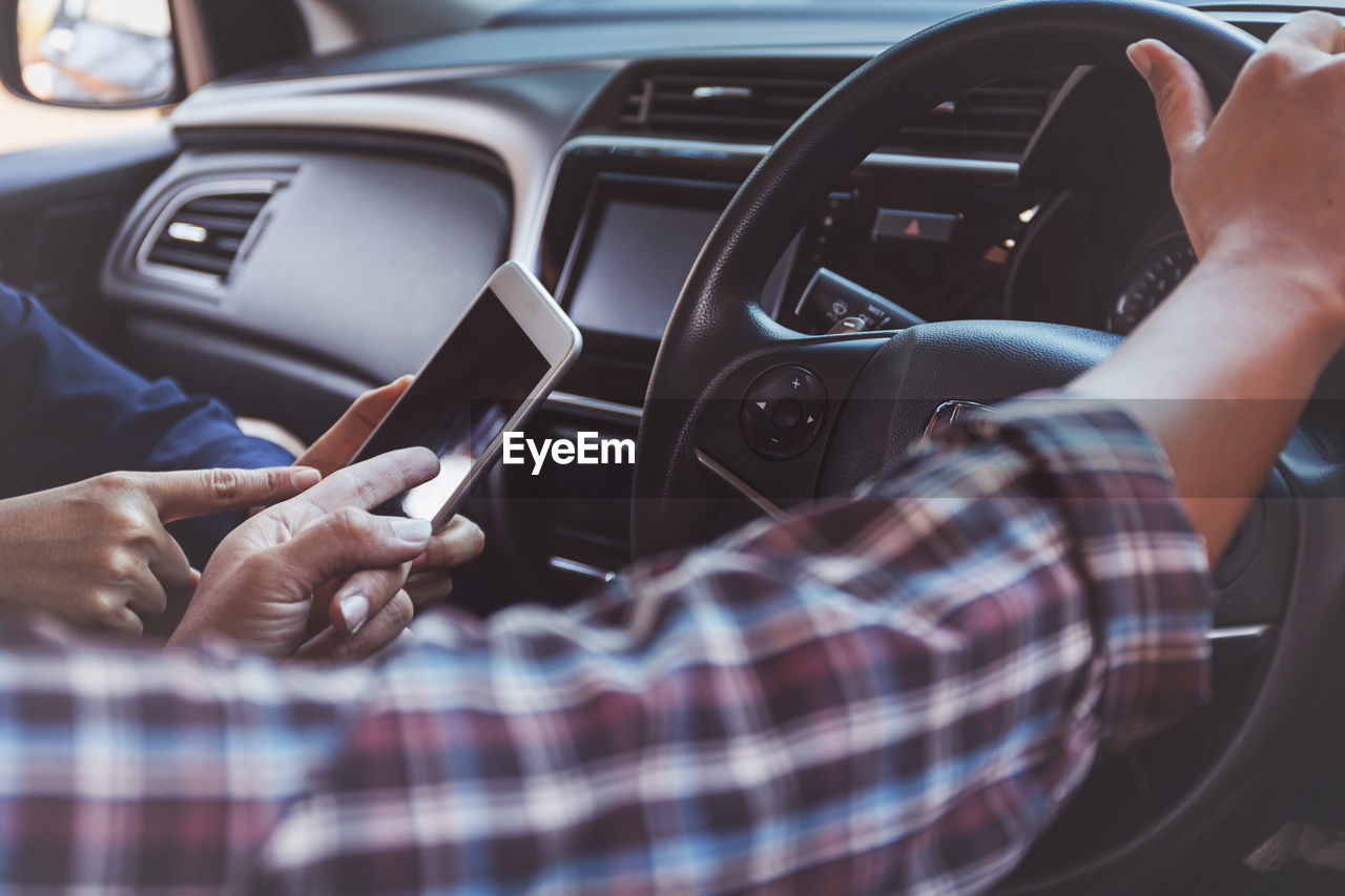 Cropped image of friends using mobile phone while sitting in car