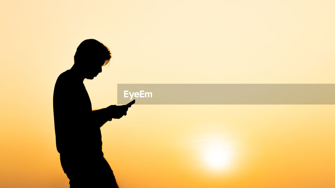 SIDE VIEW OF SILHOUETTE MAN STANDING AGAINST SKY DURING SUNSET