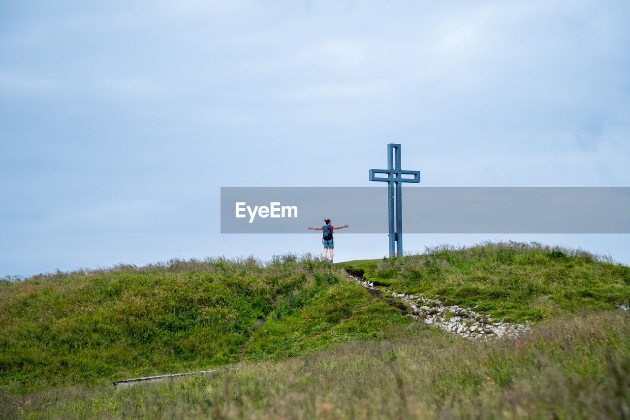 Woman standing next to crucifix on alpine footpath in the austrian alps, loser mountain region