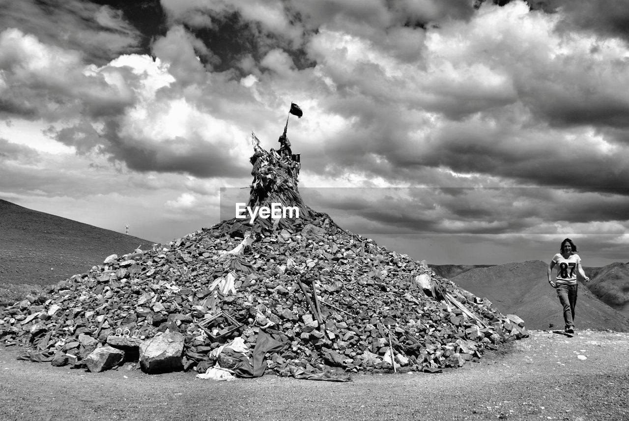 Woman walking on mountain against cloudy sky