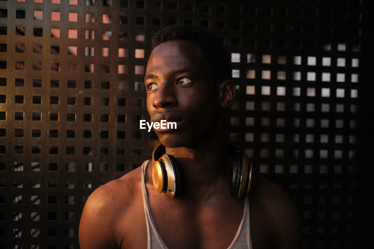 Thoughtful young man with headphones around neck looking away while at gym