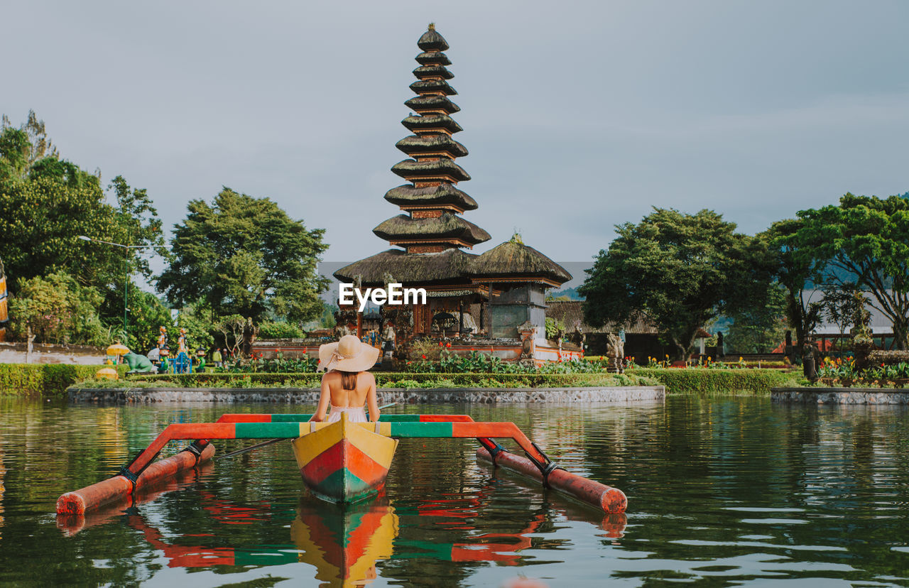 Woman in outrigger at pura ulu danau temple against sky