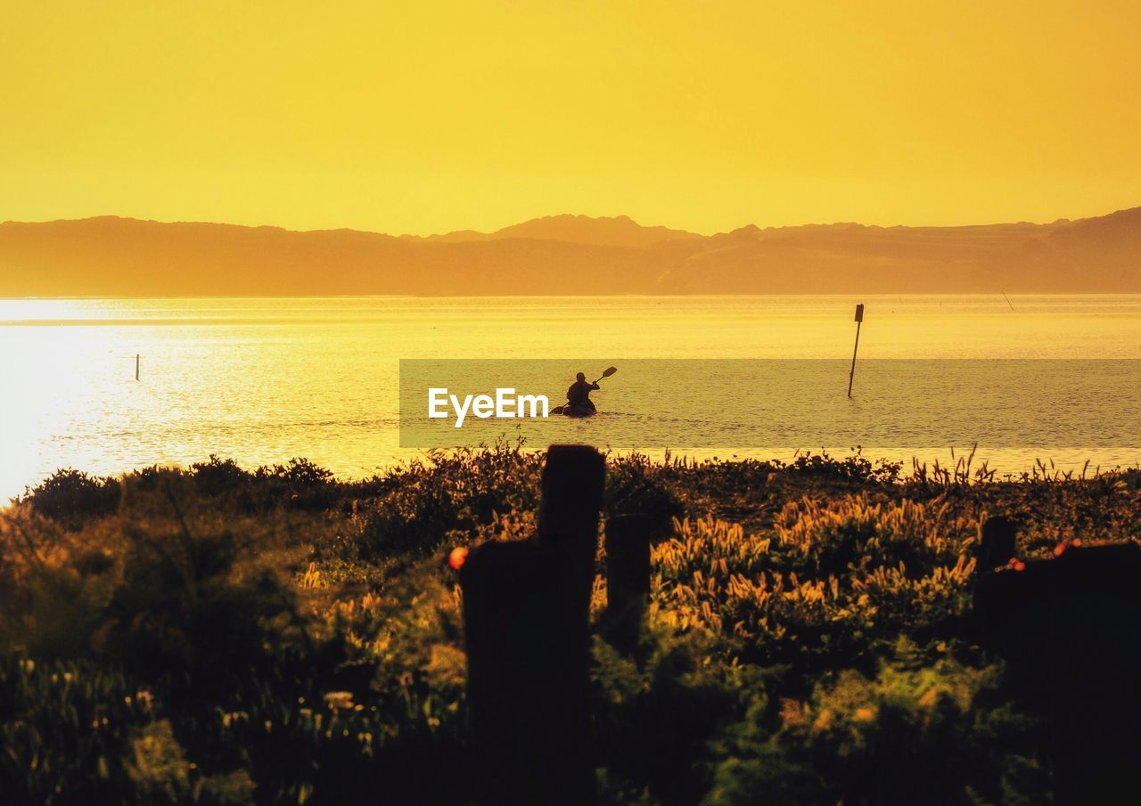 Person oaring boat in lake against sky during sunrise