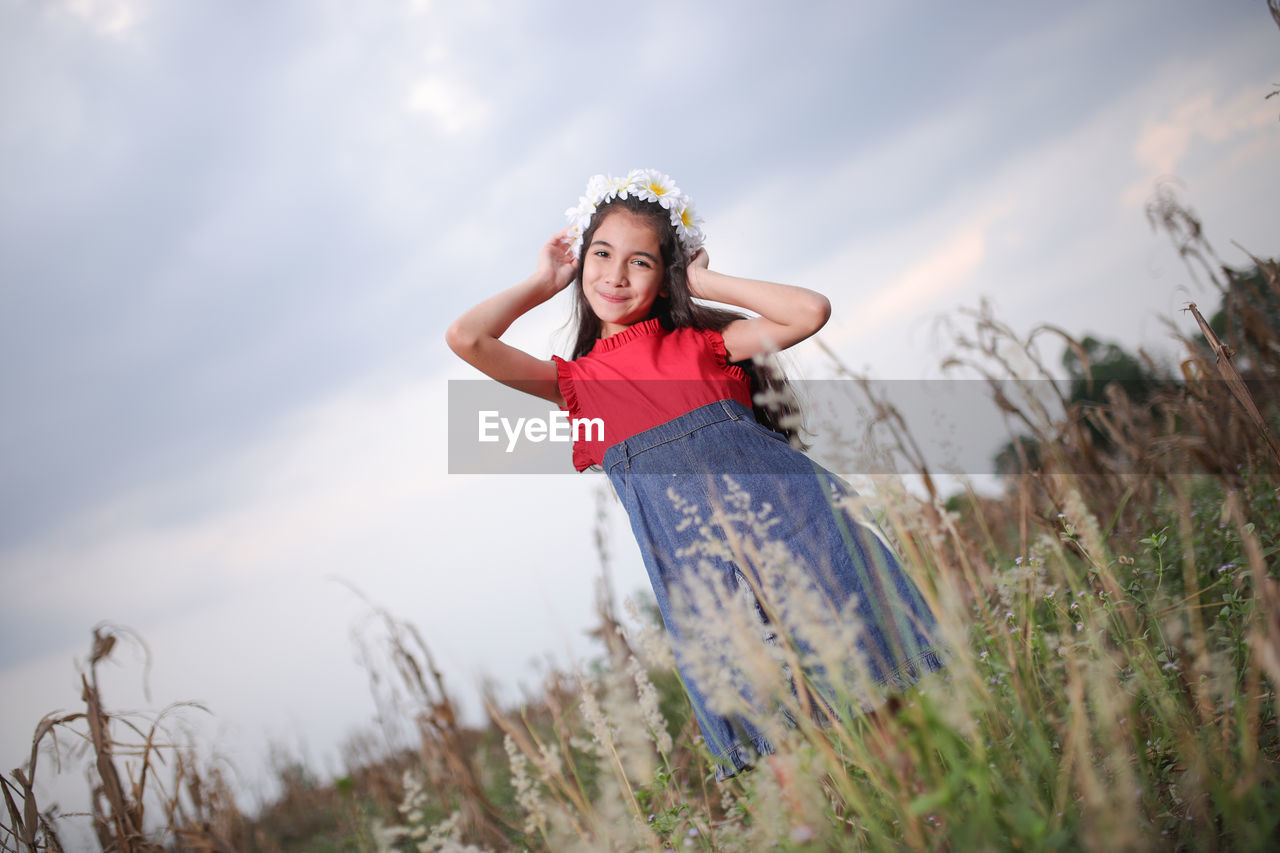 Portrait of smiling cute girl standing amidst plants on field during sunset