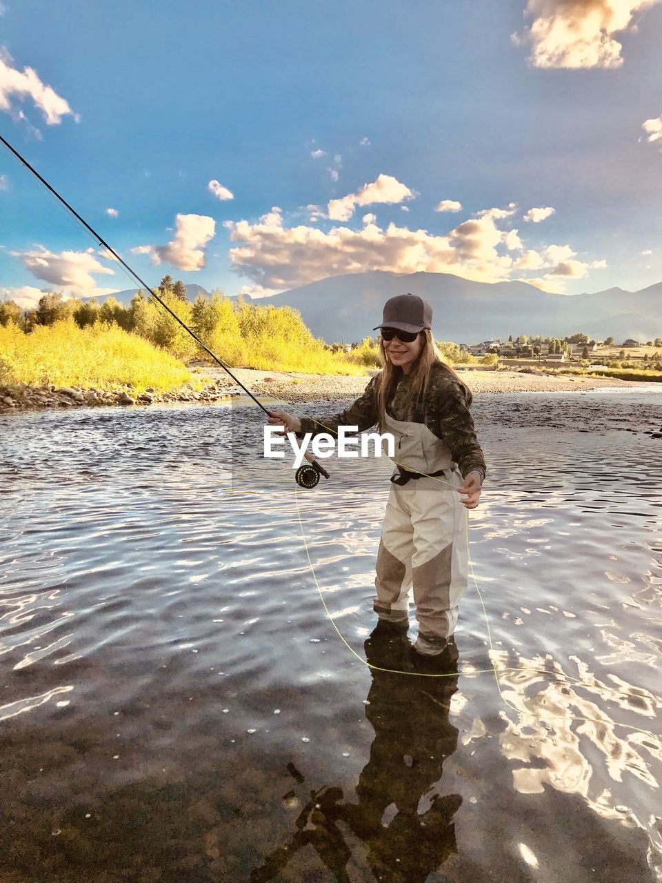 Full length of woman fishing at river against sky