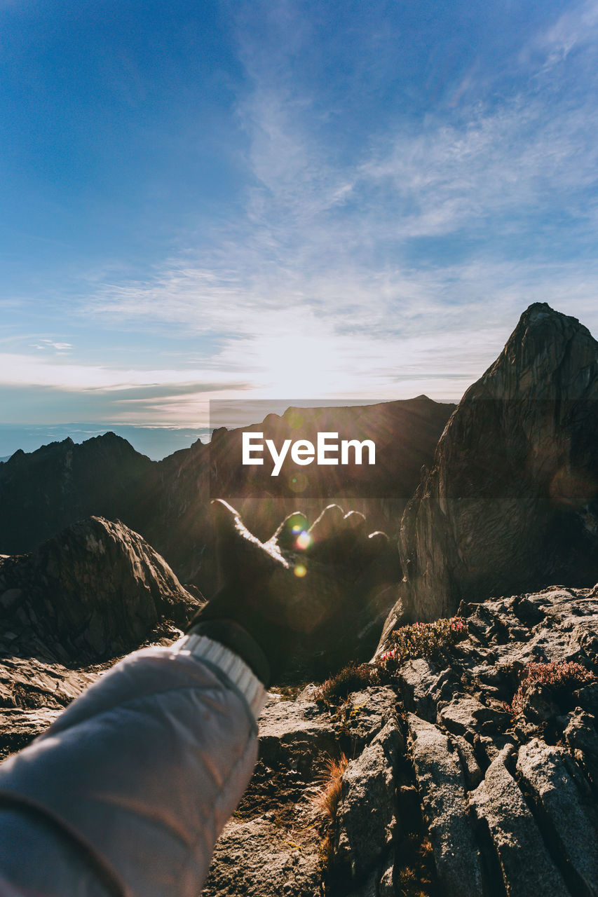 MIDSECTION OF PERSON ON ROCK AGAINST SKY