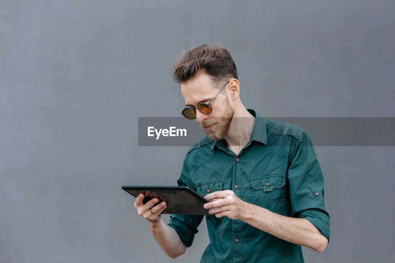 A young man in sunglasses holds a tablet in his hands and reads information on the tablet