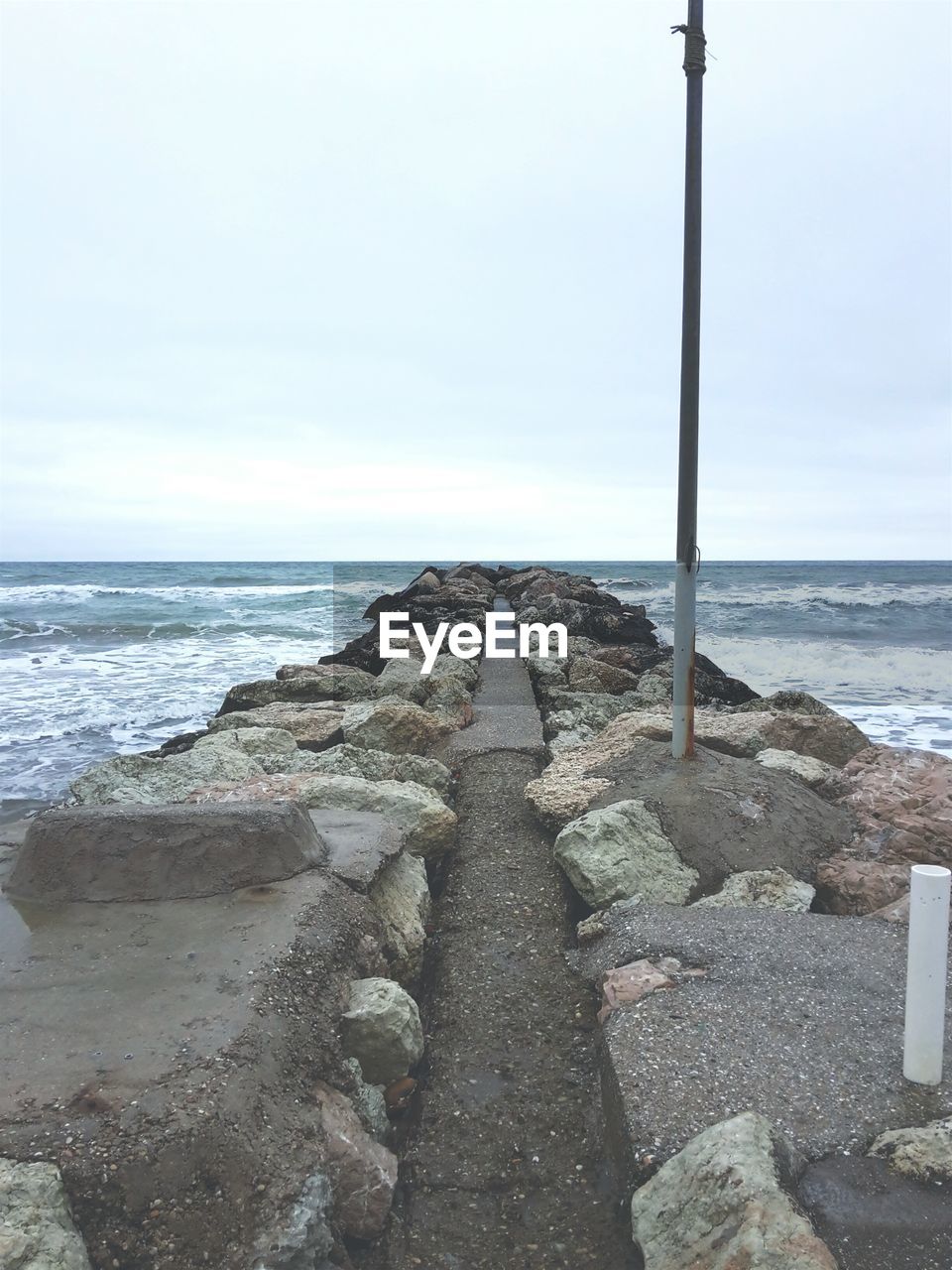 Rocky walkway amidst sea against sky