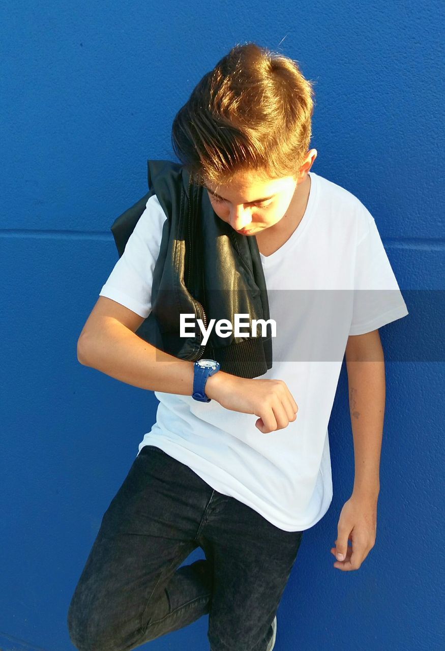 Boy checking time while leaning on blue wall