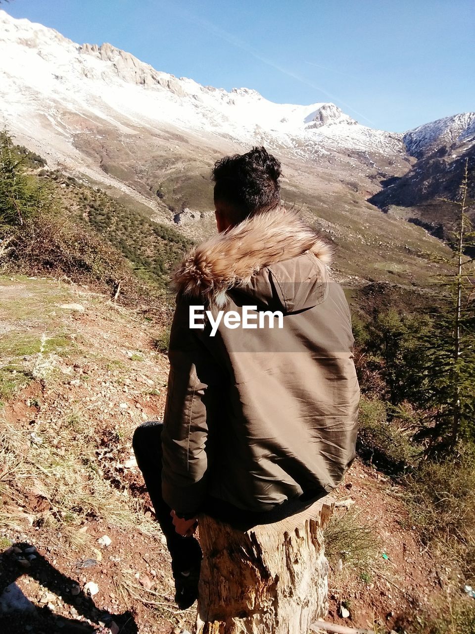 Rear view of man sitting on mountain against sky