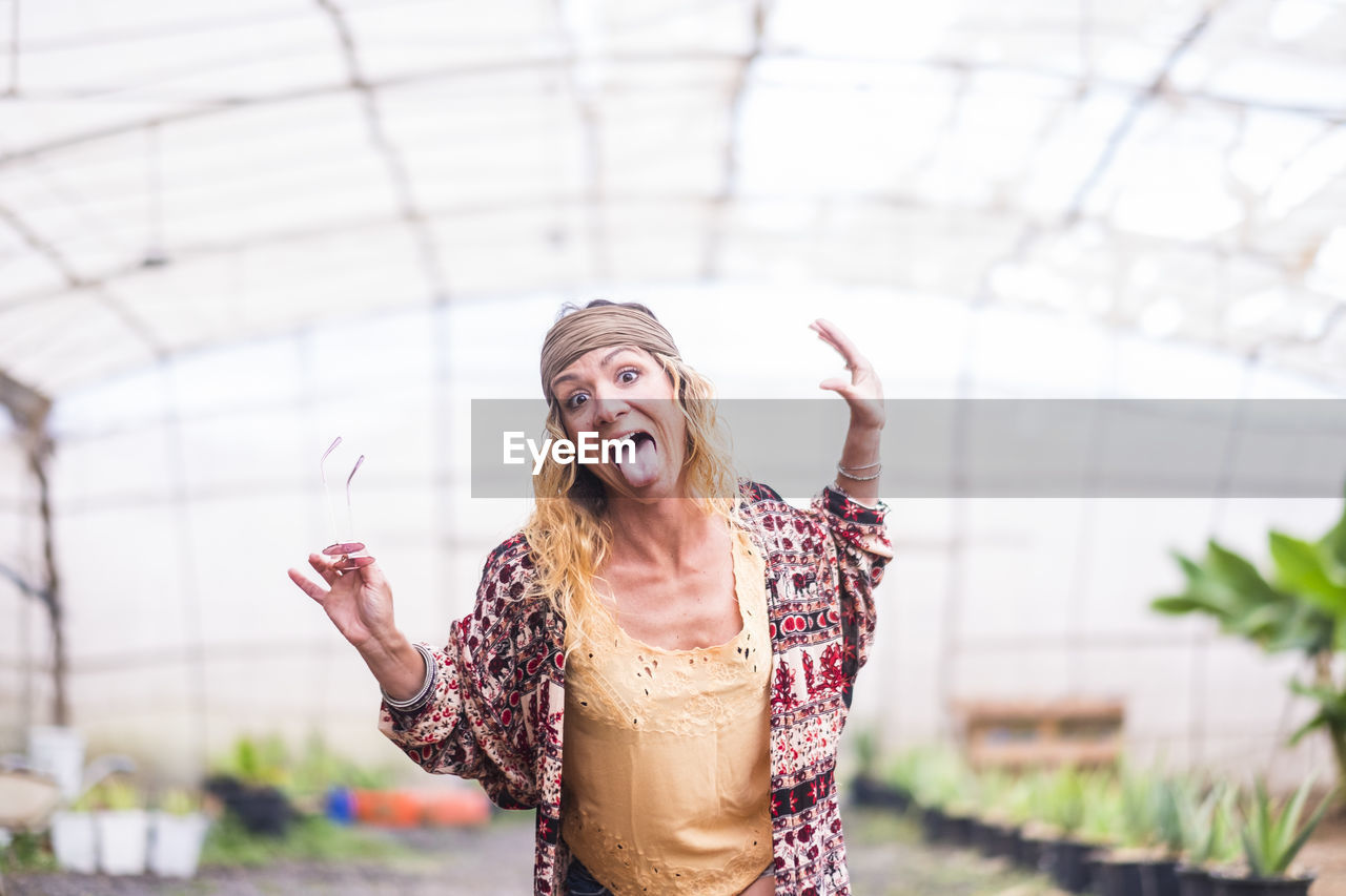 Portrait of woman making face while standing at greenhouse