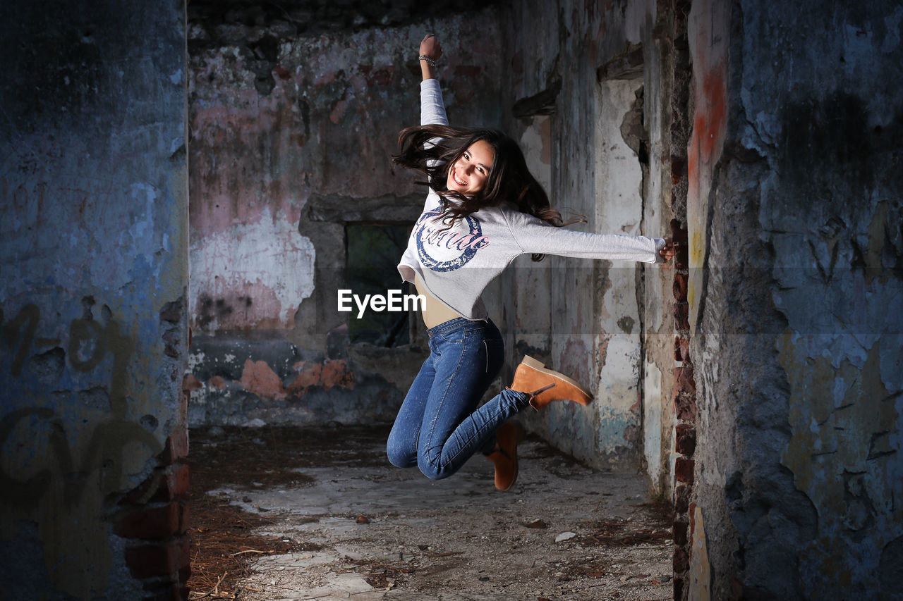 Portrait of young woman jumping at abandoned building