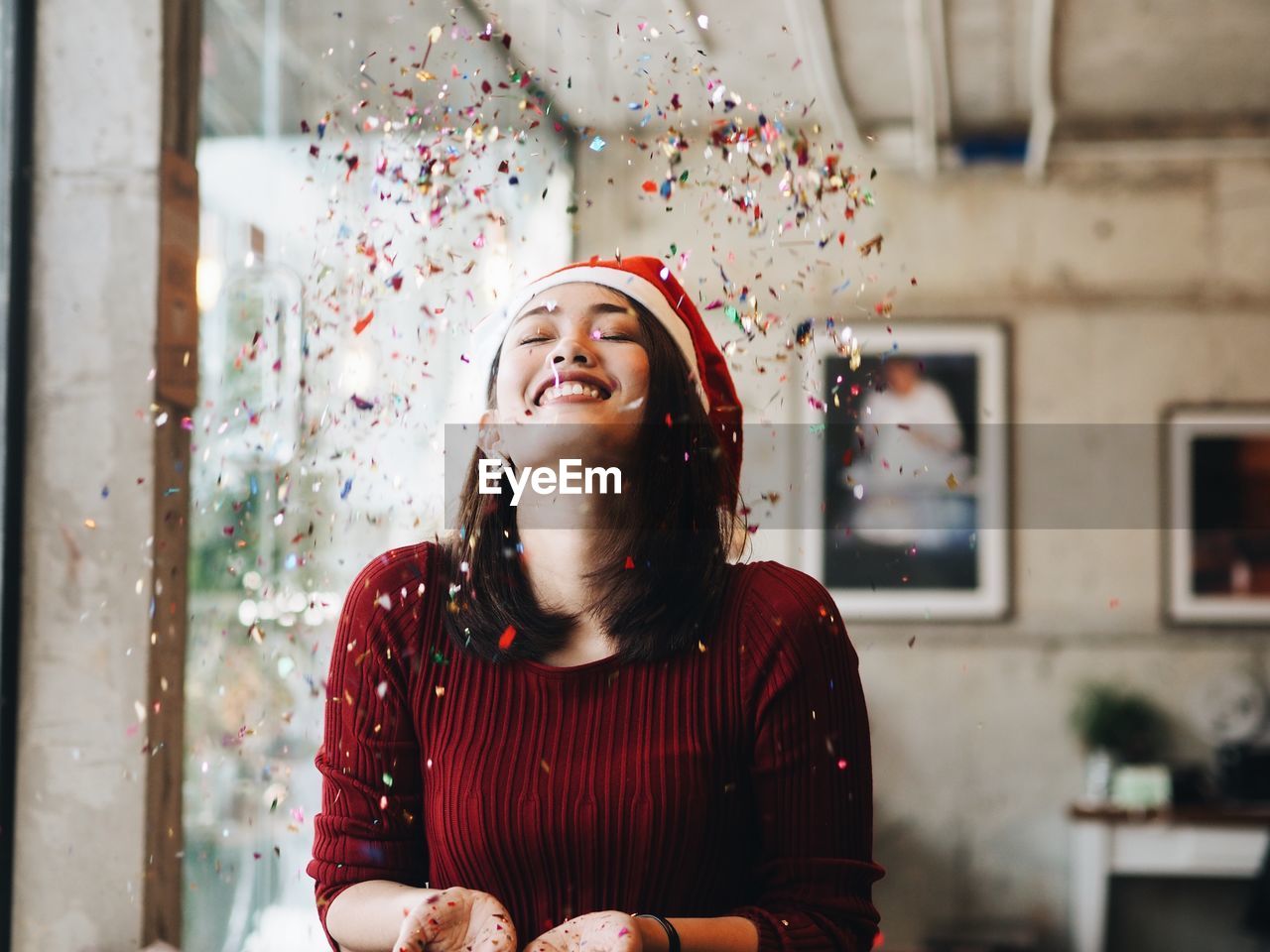 Close-up of smiling young woman throwing confetti while standing at home during christmas